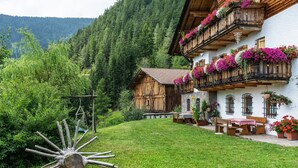 Un chalet traditionnel en bois, doté de balcons ornés de fleurs, niché dans une vallée verdoyante, avec des montagnes en toile de fond.
