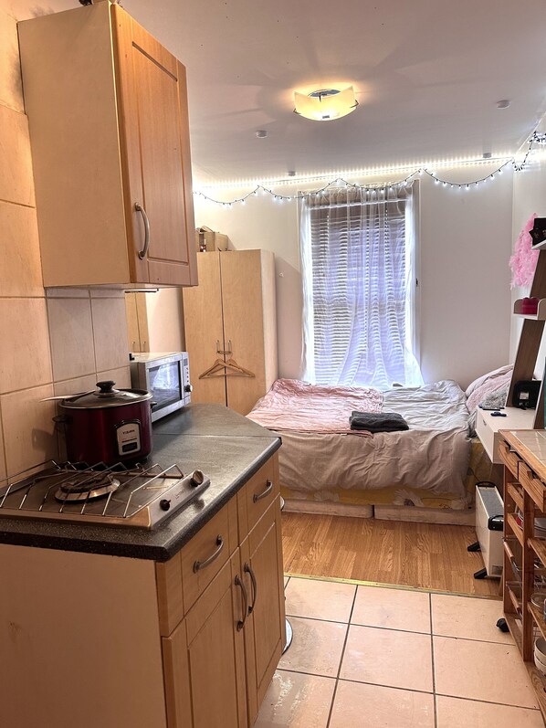 Cozy retreat with a kitchenette, stove, microwave, and refrigerator. The room features a bed with a blanket and a window with sheer curtains.