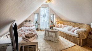 A cozy attic bedroom with a bed, a wicker sofa, a small round table, and a radiator.