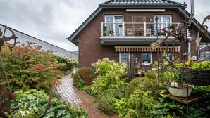 A two-story house with a brick exterior, a balcony, and a garden with various plants and a pathway.