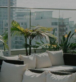 Enjoy the urban view from this balcony with a sofa and side table, surrounded by potted plants.