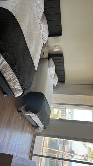 Quarto com cama, mesa de cabeceira, janela e vista para edifícios.