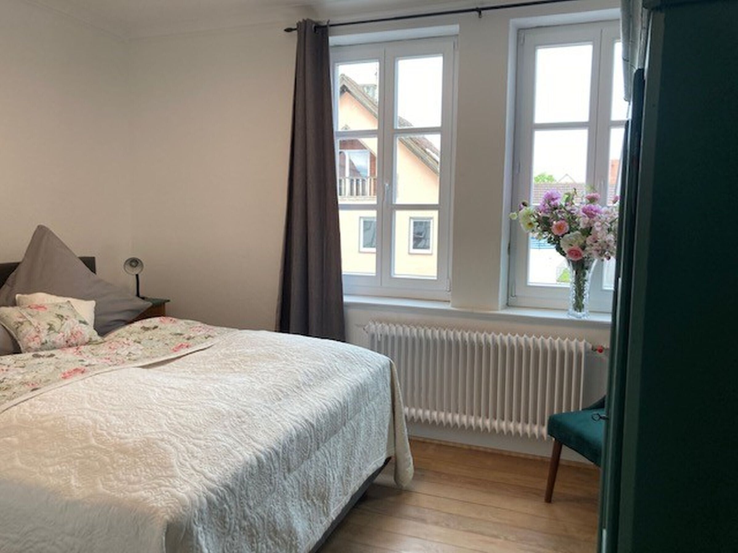 Une chambre à coucher avec un lit, une fenêtre avec des rideaux, un radiateur et une chaise.