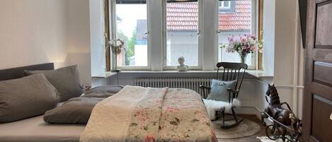A bedroom with a bed, a chair, a radiator, and a window with a view of buildings.