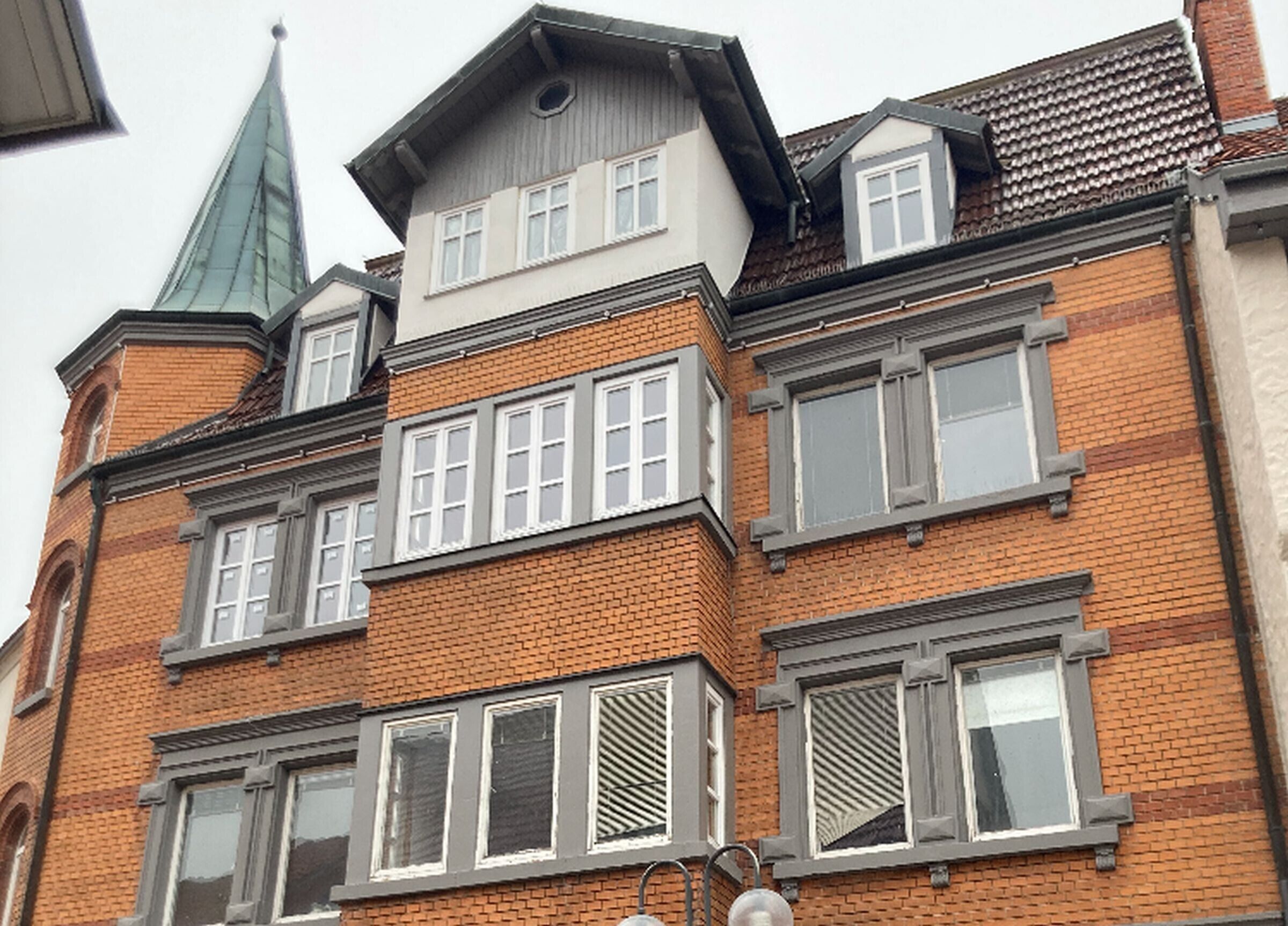 Un edificio de varios pisos con fachada de ladrillo, múltiples ventanas y techo de tejas verdes.