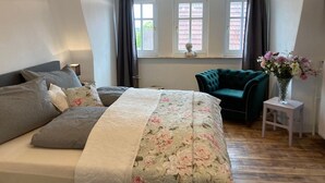 Une chambre à coucher avec un lit, une chaise, une table de chevet et une fenêtre avec des rideaux.
