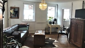 Ein Wohnzimmer mit einer Ledersofa, einer Chandelier, einem Holzkabinett und einem Schreibtisch mit einem Computer.