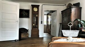 Ein Korridor mit Holzdielen, einer alten Standuhr, einem Antiquitäten Tisch und einer Tür zu einem anderen Raum.