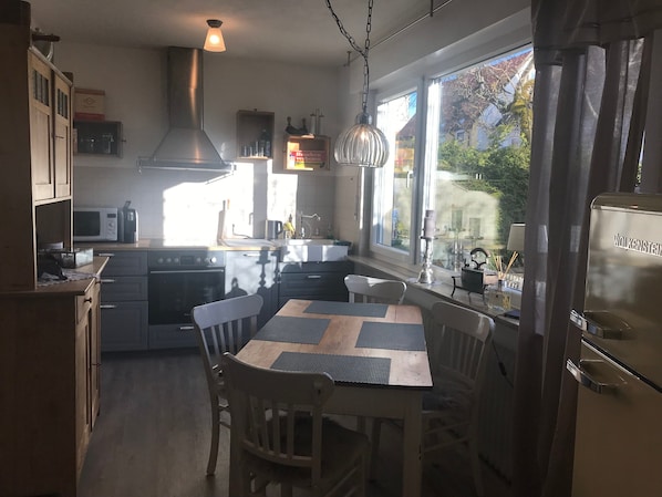 Une cuisine équipée d’une cuisinière, d’un four à micro-ondes et d’un évier, une table à manger avec des chaises, et une vue par la fenêtre.