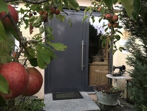 Une porte de couleur sombre, un pot de fleurs en métal contenant des plantes et une machine à coudre ancienne posée sur une table.