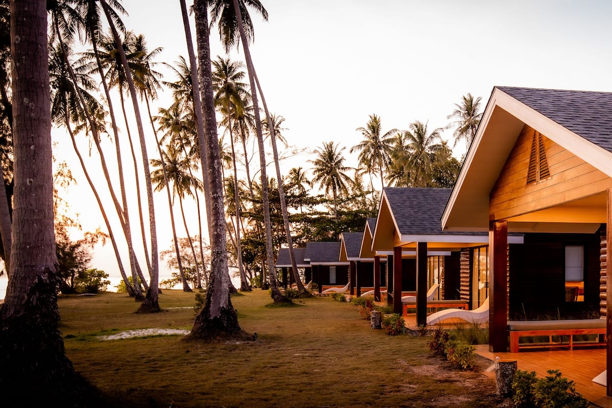 A resort with multiple wooden cabins, each featuring a balcony and a view of the surrounding palm trees.