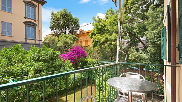 A balcony with a table and chairs, surrounded by lush greenery and a building with a yellow facade. - Apartment 'Oceane Paradise- Charlot' with Sea View, Balcony and Wi-Fi (Levanto)