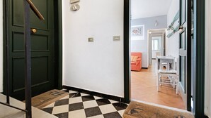 A hallway with a checkered floor, a green door, a welcome sign, and a glimpse of a living area with a sofa and a table. - Apartment 'Oceane Paradise- Charlot' with Sea View, Balcony and Wi-Fi (Levanto)