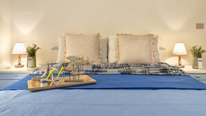 Una cama bien hecha con una colcha azul, dos almohadas decorativas y una bandeja con una estrella de mar y una taza.