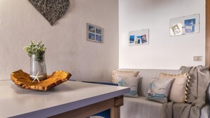 Una sala moderna con un sofá blanco, una mesa de comedor de madera y una silla azul. Hay cuadros enmarcados en la pared y una cesta tejida sobre la mesa.