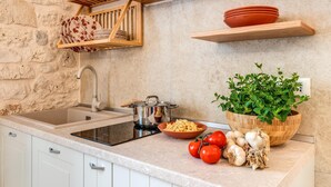 Una cocina con pared de piedra, estantes de madera, un lavabo, estufa y productos frescos.