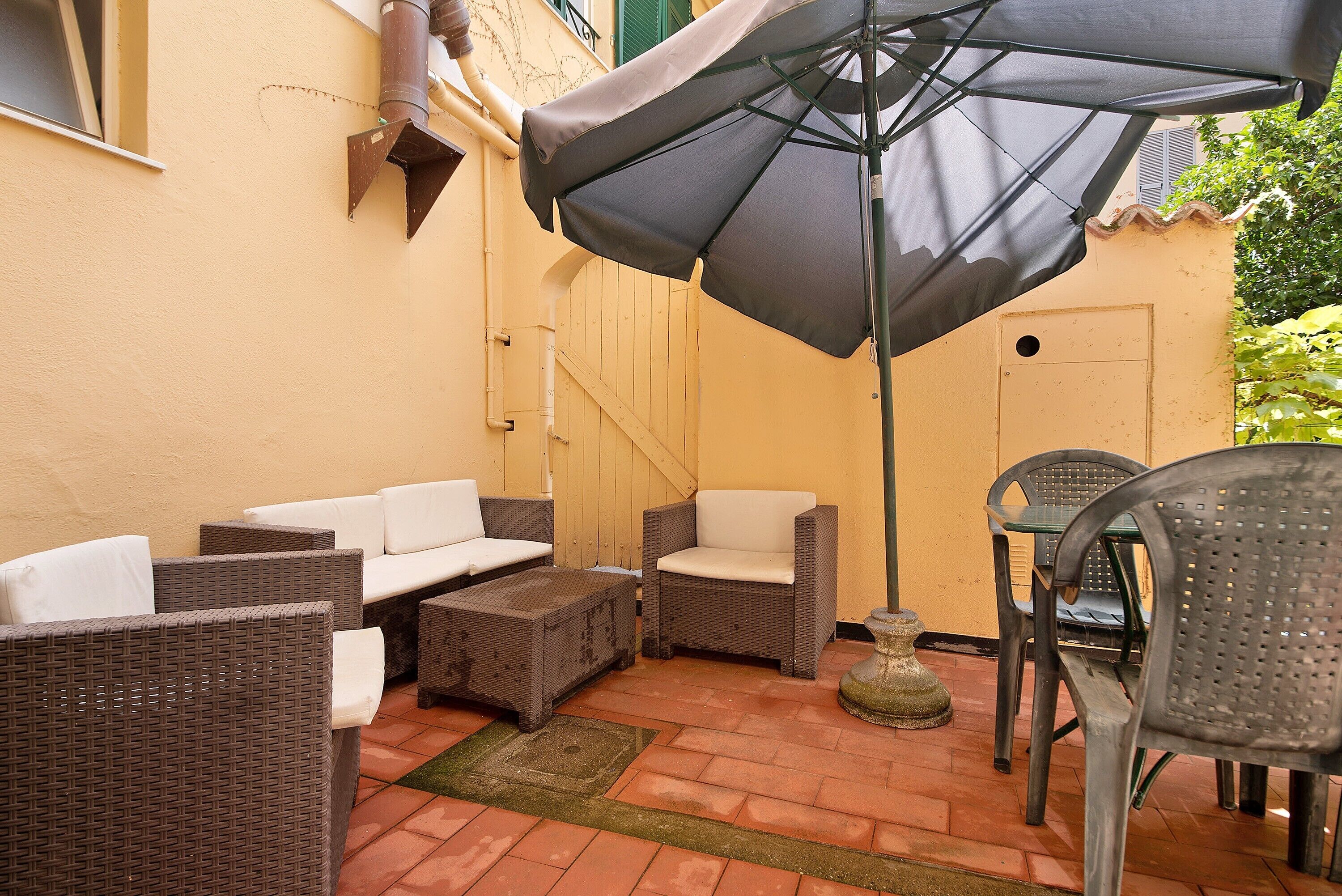 A patio with wicker furniture, a table, chairs, and a large umbrella.