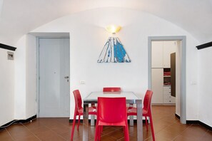 A dining area with a white table, red chairs, a wall-mounted light fixture, and a door.
