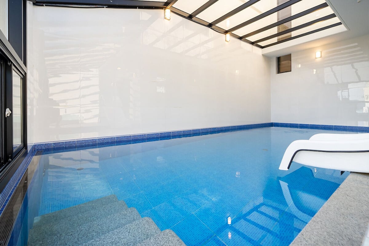 An indoor swimming pool with clear blue water, a tiled floor, and a white poolside chair.