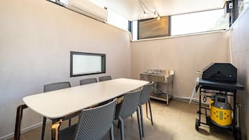 Una cocina compacta con una mesa de comedor, sillas, un lavamanos integrado, una ventana con persianas y una parrilla portátil.