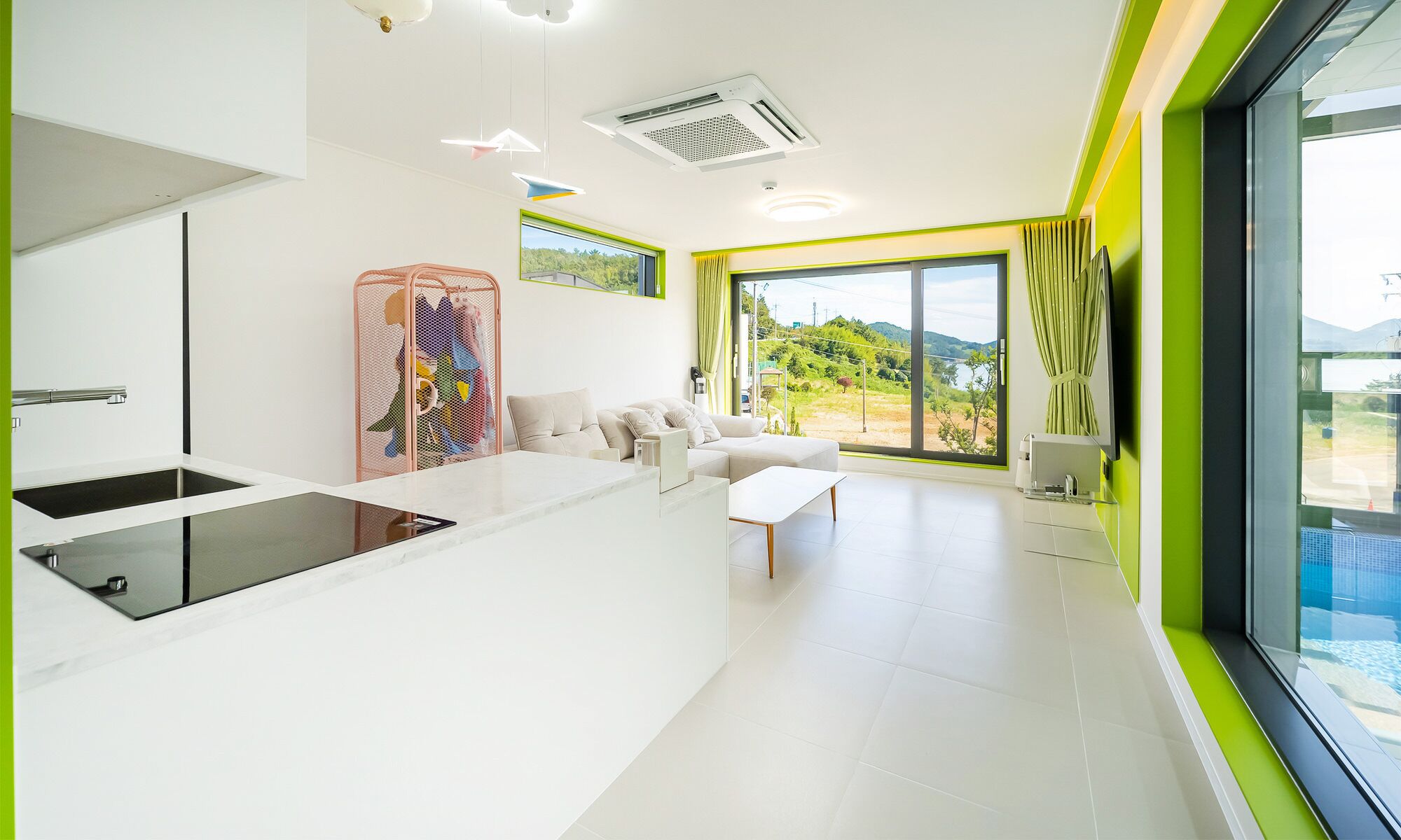 A modern living room with a sofa, a coffee table, and a large window offering a view of a pool and greenery.