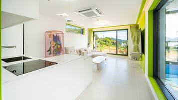 A modern living room with a sofa, a coffee table, and a large window offering a view of a pool and greenery.