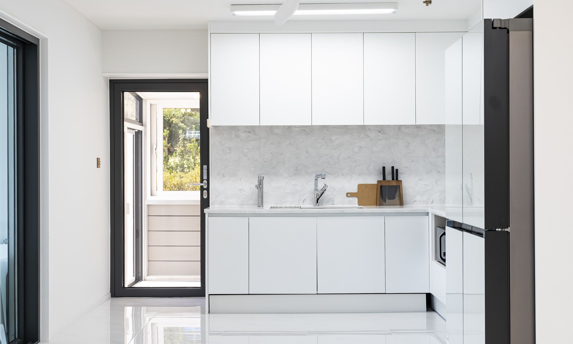 Una cocina moderna con armarios blancos, una salpicadura de mármol y un refrigerador de acero inoxidable.