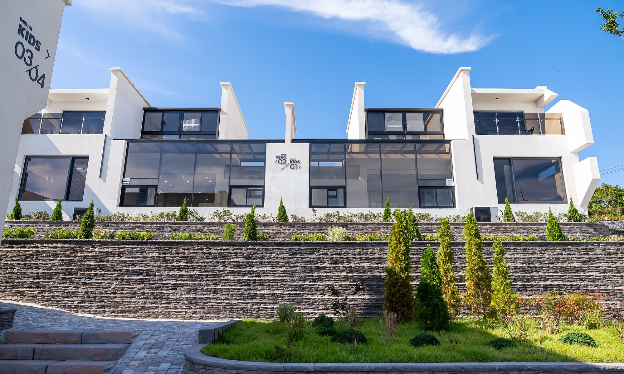 A modern building with a stone facade, large windows, and a landscaped garden area.