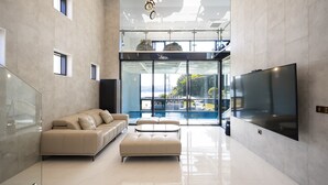 A modern living room with a sofa, ottoman, and a flat-screen TV. - Baekya Pool Villa & Kids (Yeosu)