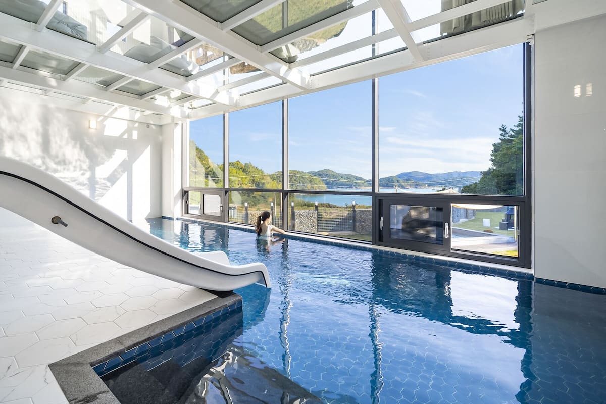 An indoor swimming pool with a glass ceiling, a slide, and a view of the landscape.