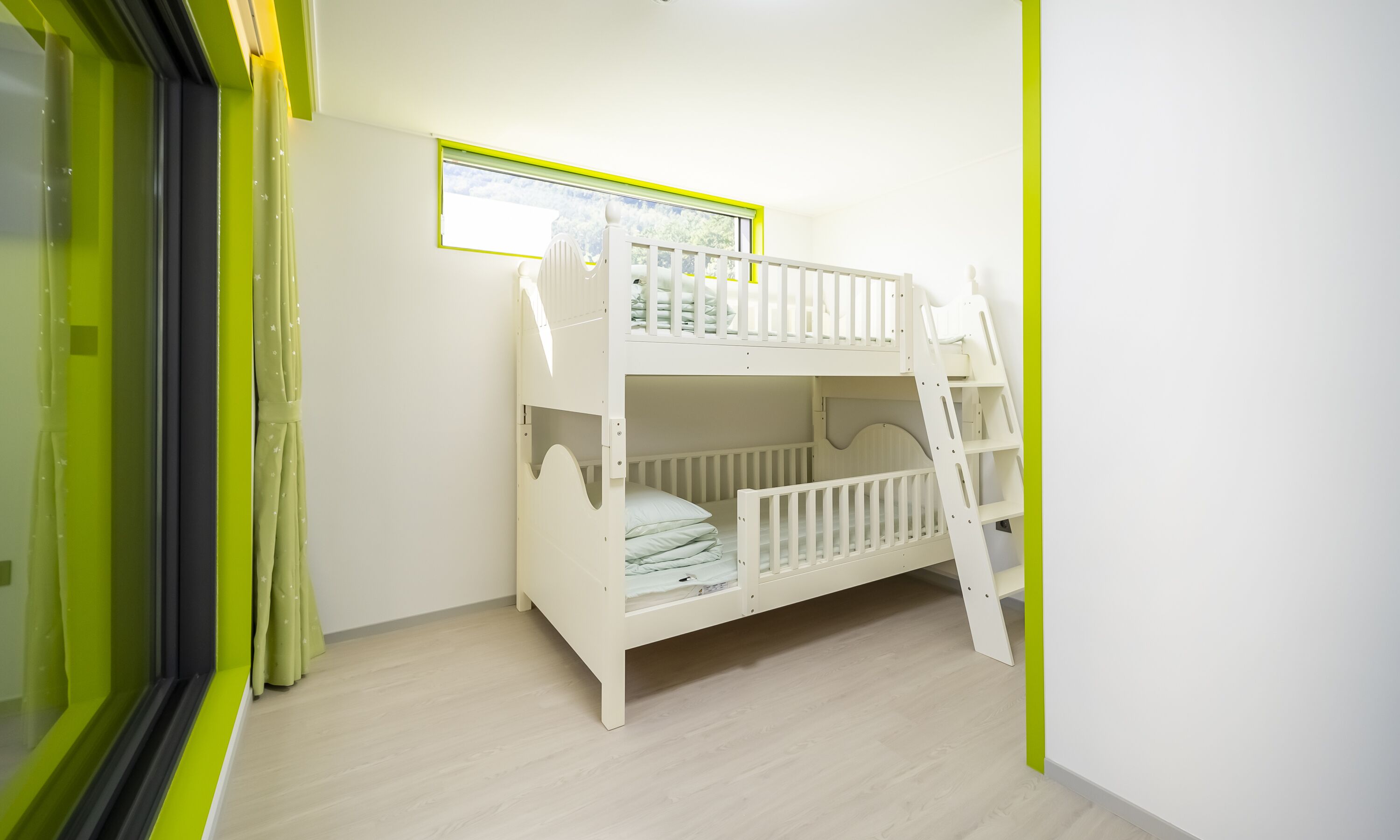 A bunk bed in a room with a window, a framed picture on the wall, and a green accent wall.
