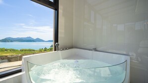 A modern bathroom with a glass-enclosed jacuzzi, a large window offering a scenic view of a lake and mountains. - Baekya Pool Villa & Kids (Yeosu)