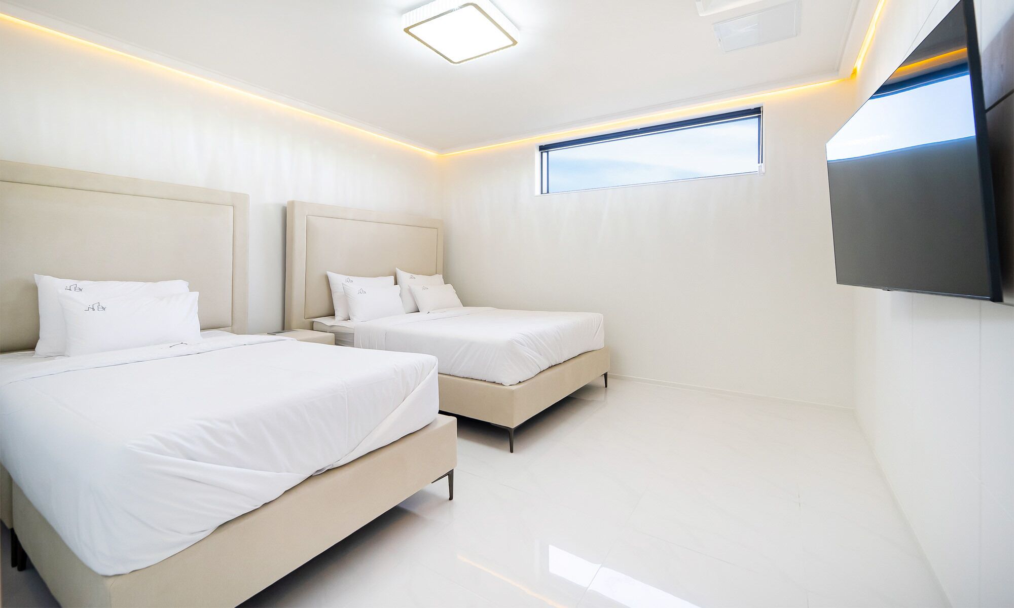 A modern bedroom with two beds, a large window, and a flat-screen TV.