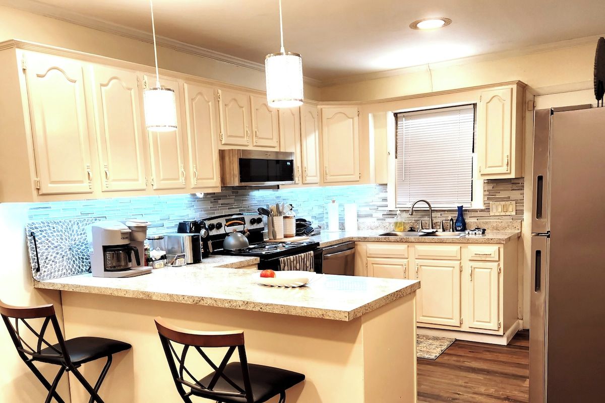 A kitchen with a central island, bar stools, a microwave, stove, and a refrigerator.