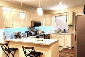 A kitchen with a central island, bar stools, a microwave, stove, and a refrigerator. - Byrd Nest @ Coventry · 3BR/2BA Home |Near Hospital, Downtown & US64/I-95 (Rocky Mount)