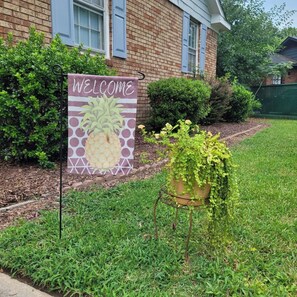 A welcome sign with a pineapple design, a brick building, and a potted plant in the foreground. - Byrd Nest @ Coventry · 3BR/2BA Home |Near Hospital, Downtown & US64/I-95 (Rocky Mount)