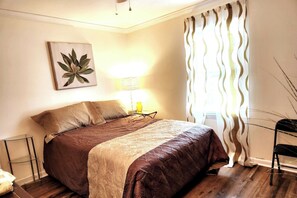 A bedroom with a bed, a bedside lamp, a wall-mounted artwork, and a window with curtains. - Byrd Nest @ Coventry · 3BR/2BA Home |Near Hospital, Downtown & US64/I-95 (Rocky Mount)