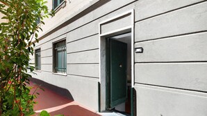 Un bâtiment avec un chemin en briques, une porte verte et une fenêtre ornée d’une grille en métal.