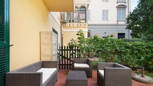 Une terrasse extérieure avec des meubles en osier, un mur jaune et un portail noir.