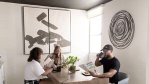 Un espace repas moderne avec une table en bois, des chaises grises et un grand tableau abstrait accroché au mur.