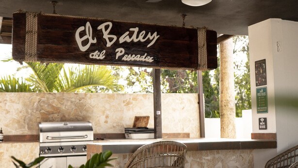 Un espace cuisine extérieur dot é d’un ventilateur de plafond, d’une enseigne indiquant « El Batey el Piscadero » et d’un mur en pierre en arrière-plan.