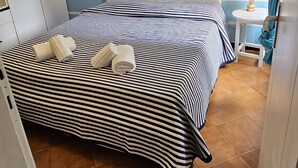 Een slaapkamer met een gestreept beddegoed, een wit hoofdeinde, een klein nachtkastje met een lamp, en een wanddecoratie van de Italiaanse vlag.