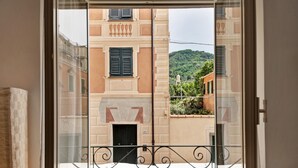 A balcony with a wrought iron railing, a door with a number plate, and a view of a building with a bell tower and greenery. - Apartment 'Oceane Paradise - Churchill' with Sea View, Balcony and Wi-Fi (Levanto)