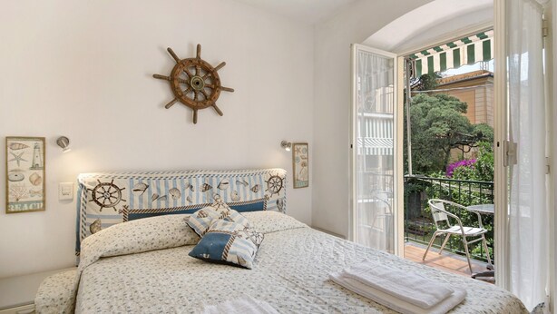 A bedroom with a nautical-themed headboard, a balcony with a view of greenery and a chair, and a bed with a patterned bedspread. - Apartment 'Oceane Paradise - Churchill' with Sea View, Balcony and Wi-Fi (Levanto)
