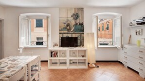A room with a TV on a white stand, open windows with shutters, a white dresser, and a tiled floor. - Apartment 'Oceane Paradise - Churchill' with Sea View, Balcony and Wi-Fi (Levanto)