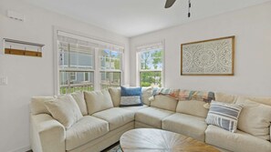 A living room with a beige sectional sofa, a round coffee table, and a decorative wall piece.