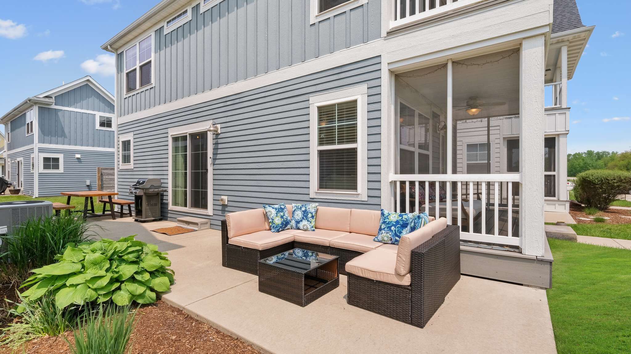 A two-story house with a covered porch, outdoor furniture, and a grill.