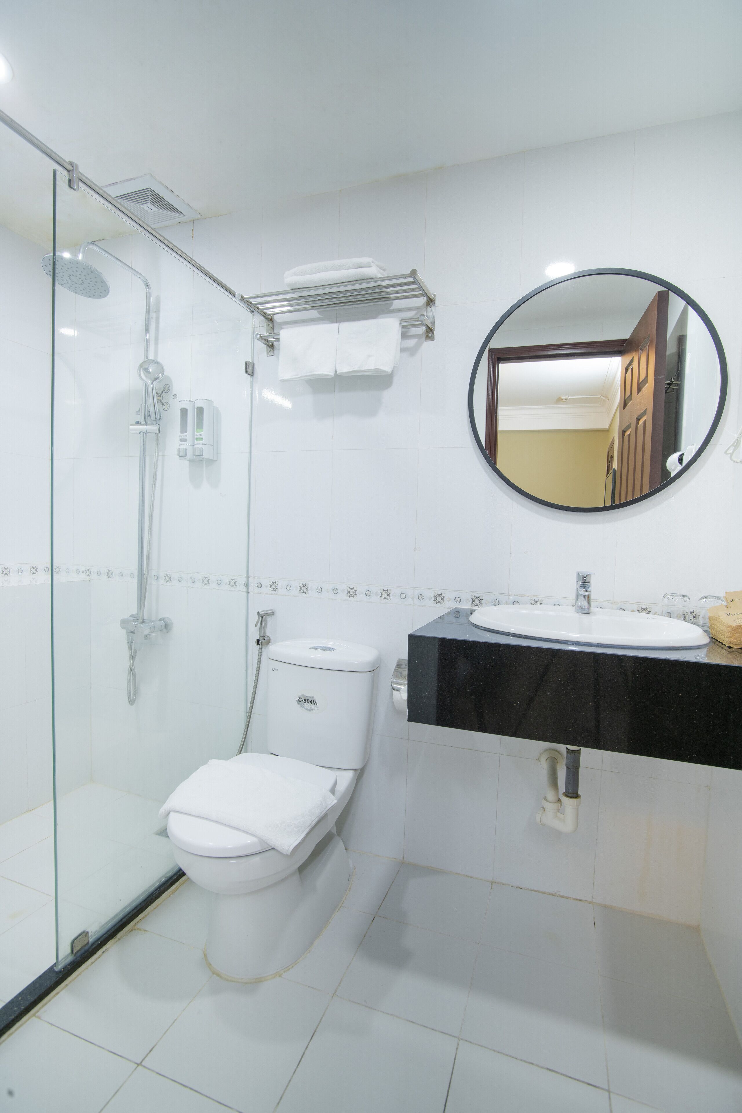 Een badkamer met een douchecabine van glas, een wit toilet, een zwarte wastafel en een ronde spiegel.