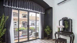 Een kamer met een schuifdeur naar een balkon, een donker houten consoletafel met een spiegel, en twee planten in potten.
