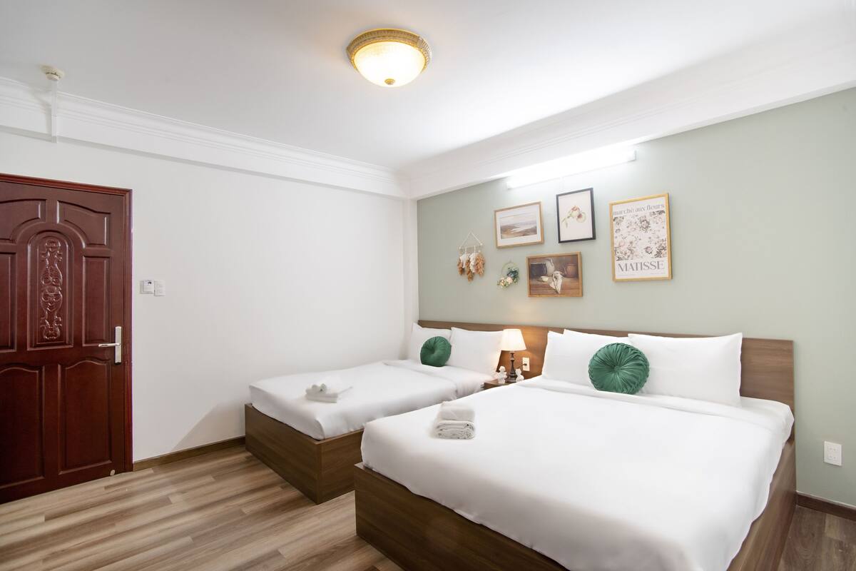 Ein Hotelzimmer mit zwei Betten, einer Holztür und einer Wand mit gerahmten Kunstwerken.